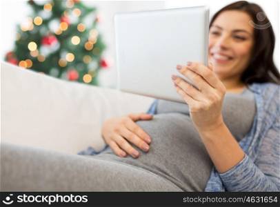 pregnancy, holidays, technology, people and expectation concept - close up of happy pregnant woman with tablet pc computer over christmas tree background
