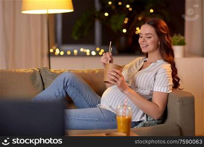 pregnancy, leisure and people concept - happy smiling pregnant woman on sofa watching tv and eating takeaway wok food with chopsticks at home. pregnant woman watching tv and eating wok at home