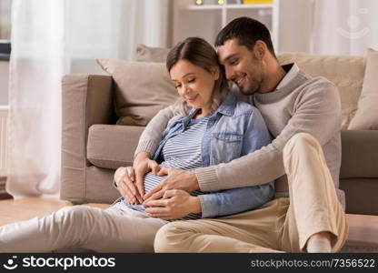 pregnancy, love and care concept - happy man hugging pregnant woman and making hand heart gesture at home. man with pregnant woman making hand heart at home