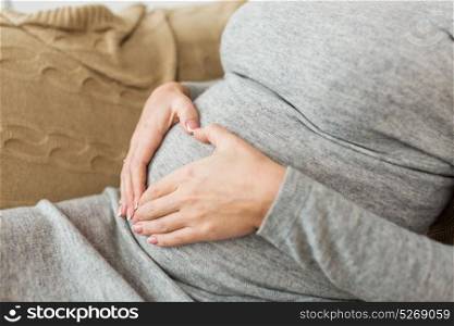 pregnancy, love and people concept - close up of pregnant woman making heart gesture on her belly. pregnant woman making heart gesture on her belly