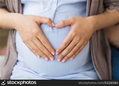 pregnancy, love and people concept - close up of pregnant woman making hand heart on belly. close up of pregnant woman making heart on belly