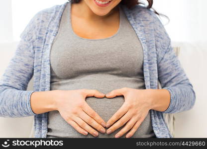 pregnancy, love, care, people and expectation concept - close up of happy pregnant woman making heart gesture at home