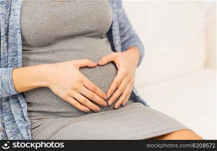 pregnancy, love, care, people and expectation concept - close up of pregnant woman belly and heart shape