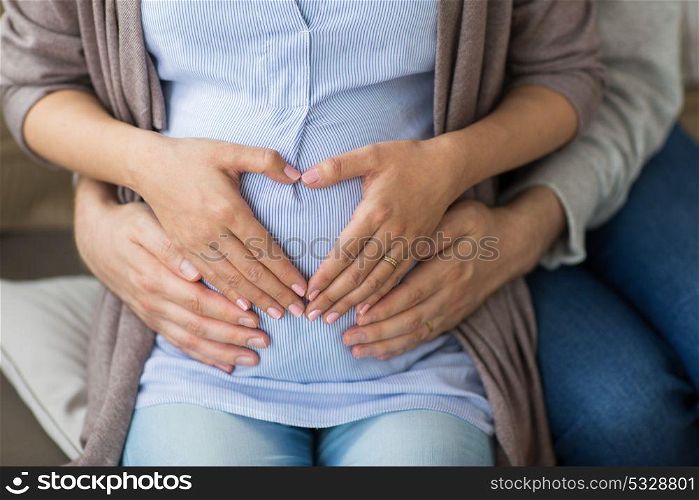 pregnancy, love, family and people concept - close up of pregnant woman making hand heart gesture on her belly. close up of pregnant woman making hand heart