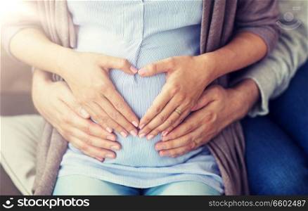 pregnancy, love, family and people concept - close up of pregnant woman making hand heart gesture on her belly. close up of pregnant woman making hand heart