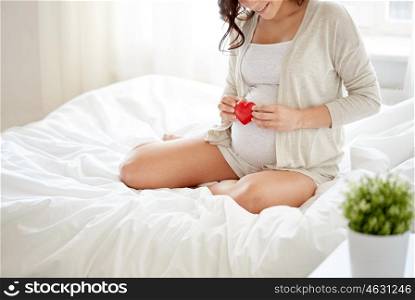 pregnancy, love, people and expectation concept - close up of happy smiling pregnant woman with red heart in bed at home bedroom
