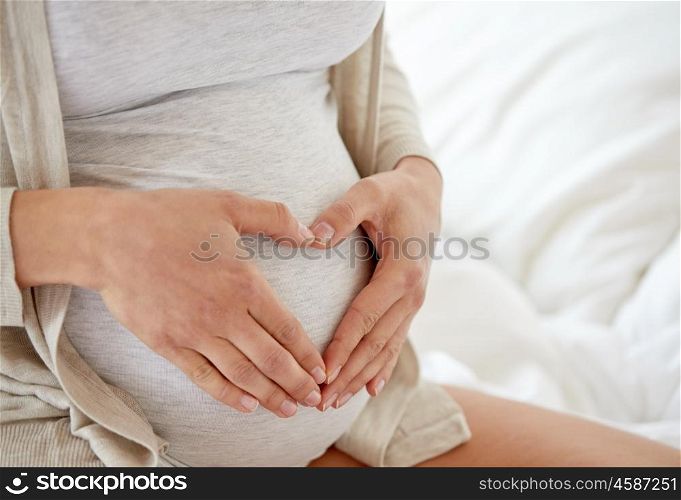 pregnancy, love, people and expectation concept - close up of pregnant woman making heart gesture in bed at home