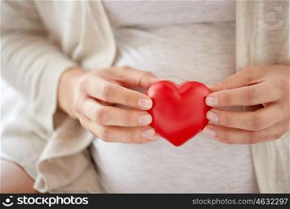 pregnancy, love, people and expectation concept - close up of pregnant woman with red heart