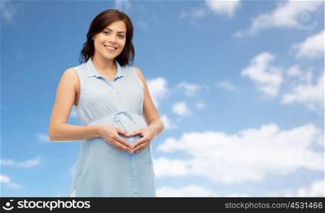 pregnancy, love, people and expectation concept - happy pregnant woman making heart gesture on belly over blue sky background