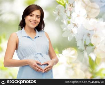 pregnancy, love, people and expectation concept - happy pregnant woman making heart gesture on belly over natural spring cherry blossom background