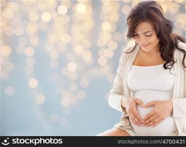 pregnancy, love, people and expectation concept - happy pregnant woman making heart gesture over holidays lights background
