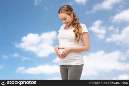 pregnancy, love, people and expectation concept - happy pregnant woman showing heart gesture over blue sky and clouds background. happy pregnant woman showing heart gesture