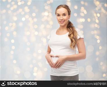 pregnancy, love, people and expectation concept - happy pregnant woman showing heart gesture over holidays lights background. happy pregnant woman showing heart gesture
