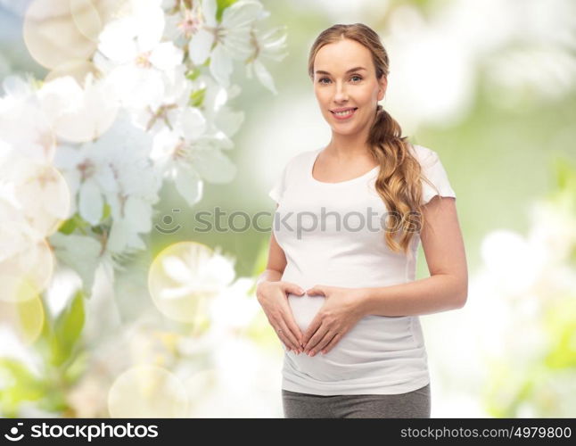 pregnancy, love, people and expectation concept - happy pregnant woman showing heart gesture over natural spring cherry blossom background. happy pregnant woman showing heart gesture