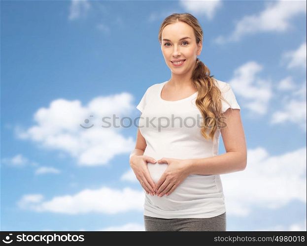pregnancy, love, people and expectation concept - happy pregnant woman showing heart gesture over blue sky and clouds background. happy pregnant woman showing heart gesture