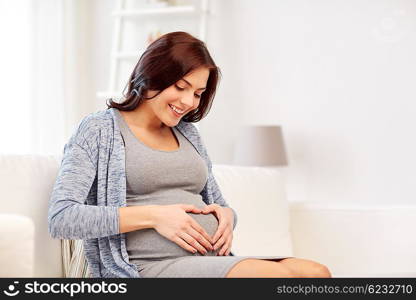 pregnancy, love, people and expectation concept - happy pregnant woman sitting on sofa and making heart gesture at home