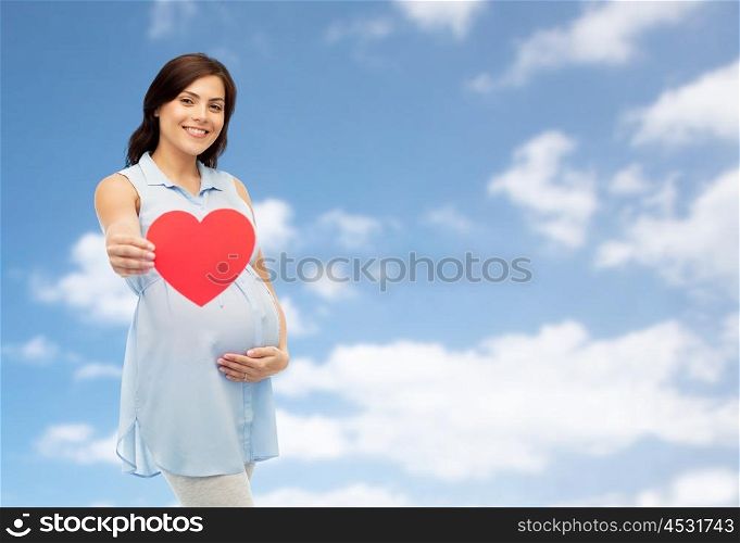 pregnancy, love, people and expectation concept - happy pregnant woman with red heart shape touching her belly over blue sky and clouds background
