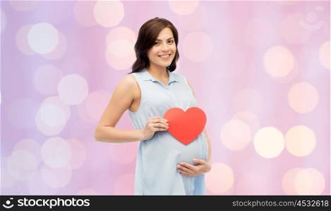 pregnancy, love, people and expectation concept - happy pregnant woman with red heart shape touching her belly over rose quartz and serenity holidays lights background