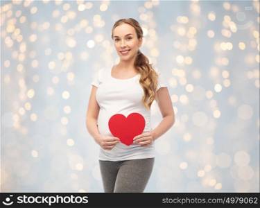 pregnancy, love, people and expectation concept - happy pregnant woman with red heart over holidays lights background. happy pregnant woman with red heart