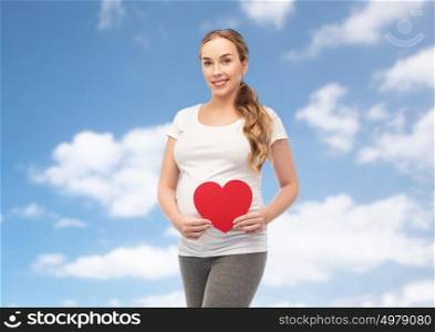 pregnancy, love, people and expectation concept - happy pregnant woman with red heart over blue sky and clouds background. happy pregnant woman with red heart