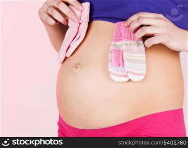 pregnancy, maternity and health concept - belly of a pregnant woman with two pairs of baby mittens