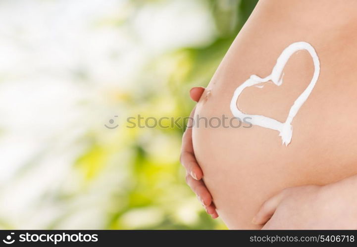 pregnancy, maternity and health concept - belly of a pregnant woman with cream and heart symbol