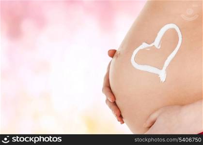 pregnancy, maternity and health concept - belly of a pregnant woman with cream and heart symbol
