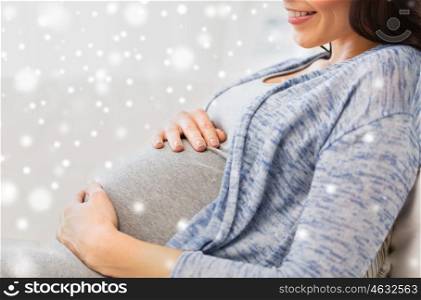 pregnancy, maternity, people, winter and expectation concept - close up of happy pregnant woman with big belly lying on sofa at home over snow