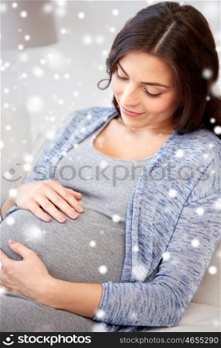 pregnancy, maternity, winter, people and expectation concept - close up of happy pregnant woman with big belly lying on sofa at home over snow