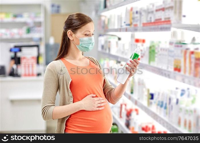 pregnancy, medicine and health concept - pregnant woman wearing protective medical mask for protection from virus disease and choosing anti stretch marks lotion at pharmacy. pregnant woman in mask choosing lotion at pharmacy