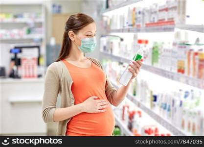 pregnancy, medicine and health concept - pregnant woman wearing protective medical mask for protection from virus disease and choosing anti stretch marks lotion at pharmacy. pregnant woman in mask choosing lotion at pharmacy