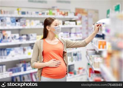 pregnancy, medicine and pandemic concept - pregnant woman wearing face protective medical mask for protection from virus disease choosing medication at pharmacy. pregnant woman in mask buys medicine at pharmacy