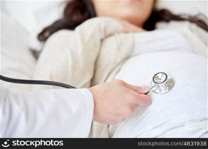 pregnancy, medicine, health care and people concept - close up of obstetrician doctor with stethoscope listening to pregnant woman baby heartbeat at hospital