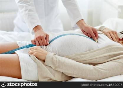 pregnancy, medicine, health care and people concept - close up of obstetrician doctor with centimeter tape measuring pregnant woman tummy at hospital