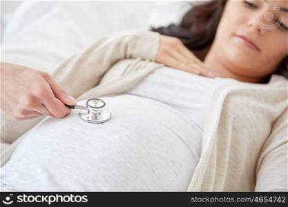pregnancy, medicine, health care and people concept - close up of obstetrician doctor with stethoscope listening to pregnant woman baby heartbeat at hospital