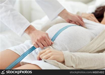 pregnancy, medicine, health care and people concept - close up of obstetrician doctor with centimeter tape measuring pregnant woman tummy at hospital