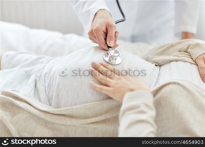 pregnancy, medicine, healthcare and people concept - close up of obstetrician doctor with stethoscope listening to pregnant woman baby heartbeat at hospital