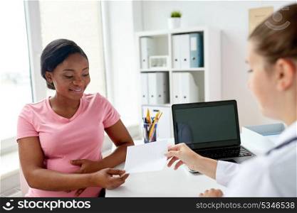 pregnancy, medicine, healthcare and people concept - gynecologist doctor giving prescription to smiling pregnant african american woman at hospital. doctor giving prescription to pregnant woman