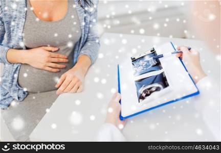 pregnancy, medicine, healthcare, winter and people concept - close up of gynecologist doctor showing ultrasound image on clipboard to pregnant woman at hospital over snow