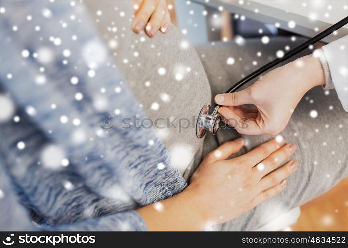 pregnancy, medicine, healthcare, winter and people concept - close up of gynecologist doctor with stethoscope listening to pregnant woman baby heartbeat at hospital over snow
