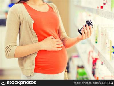 pregnancy, medicine, pharmaceutics, health care and people concept - close up of pregnant woman reading label on medication jar at pharmacy