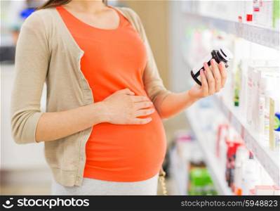 pregnancy, medicine, pharmaceutics, health care and people concept - close up of pregnant woman reading label on medication jar at pharmacy