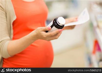 pregnancy, medicine, pharmaceutics, health care and people concept - close up of pregnant woman with prescription and medication jar reading label at pharmacy