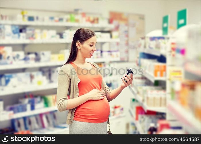 pregnancy, medicine, pharmaceutics, health care and people concept - happy pregnant woman reading label on medication jar at pharmacy