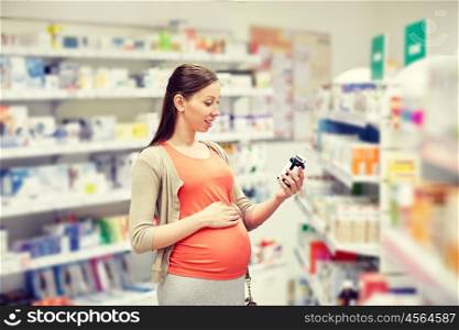 pregnancy, medicine, pharmaceutics, health care and people concept - happy pregnant woman reading label on medication jar at pharmacy