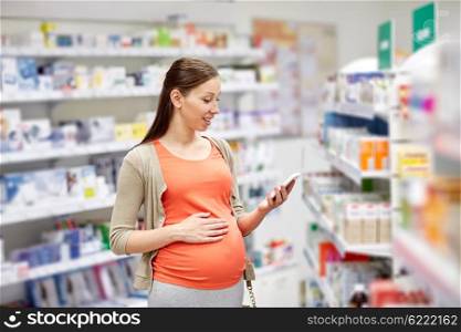 pregnancy, medicine, pharmaceutics, health care and people concept - happy pregnant woman with smartphone at pharmacy