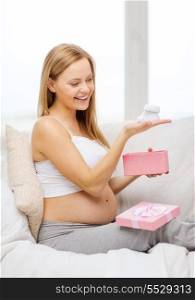 pregnancy, motherhood and celebration concept - smiling pregnant woman sitting on sofa with gift box and baby bootees