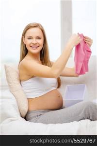 pregnancy, motherhood and celebration concept - smiling pregnant woman sitting on sofa and opening gift box with pink cardigan