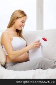 pregnancy, motherhood and celebration concept - smiling pregnant woman sitting on sofa and opening gift box