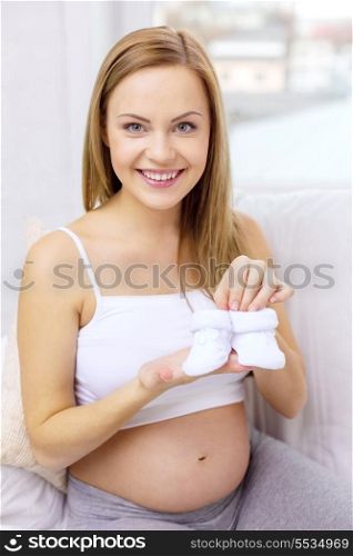pregnancy, motherhood and celebration concept - smiling pregnant woman sitting on sofa with baby bootees